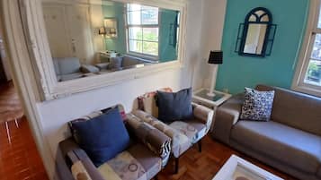 A living room with a large mirror, two sofas, a side table with a lamp, and a window with a view.