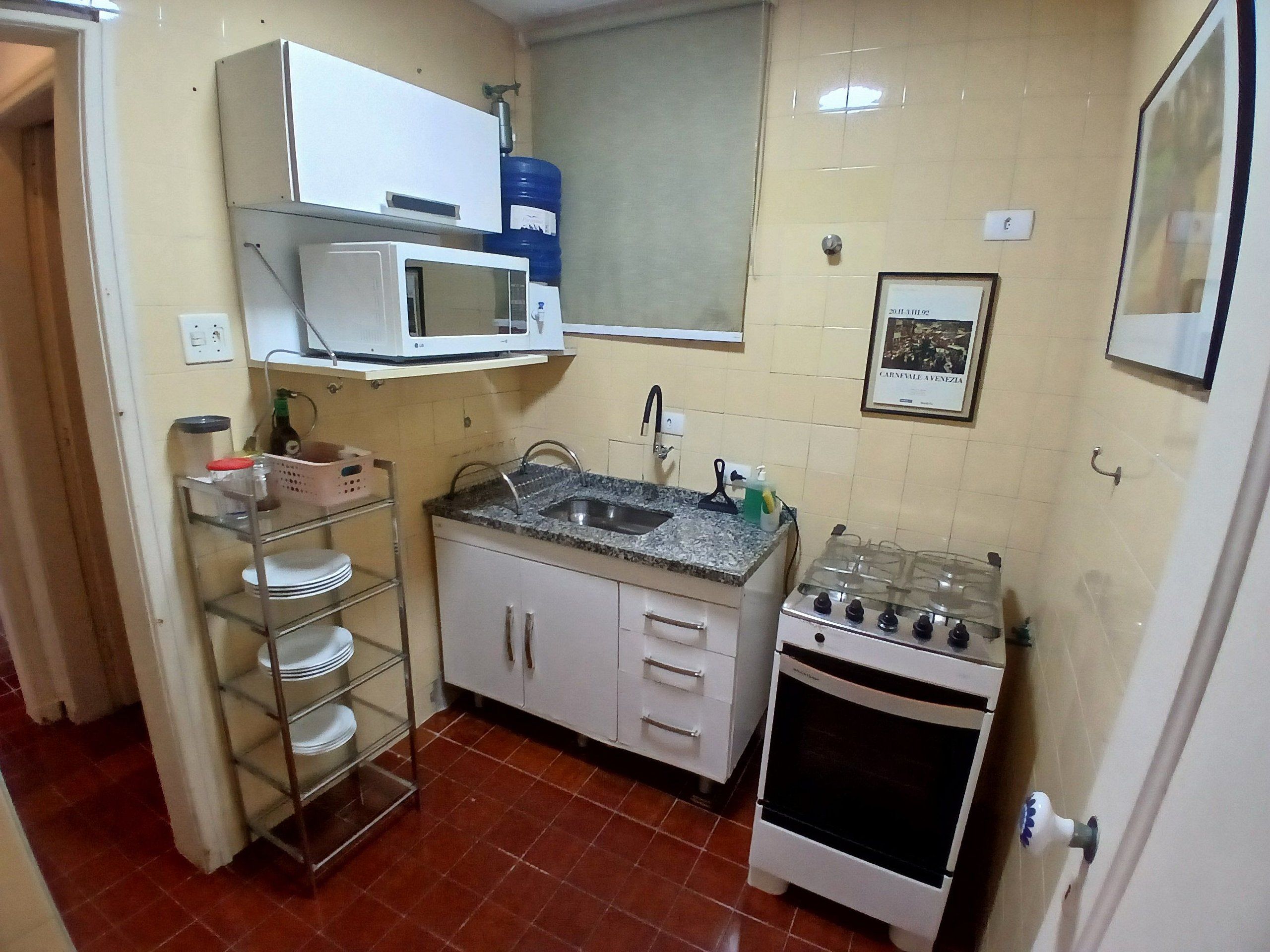 A compact kitchen with a microwave, sink, stove, and shelves with dishes.