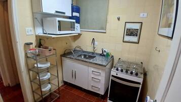 A compact kitchen with a microwave, sink, stove, and shelves with dishes.