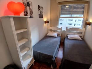 Una habitación con dos camas individuales, un armario y una ventana con persianas.