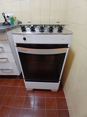 Una cocina con estufa blanca, pileta y encimera con diversos objetos.