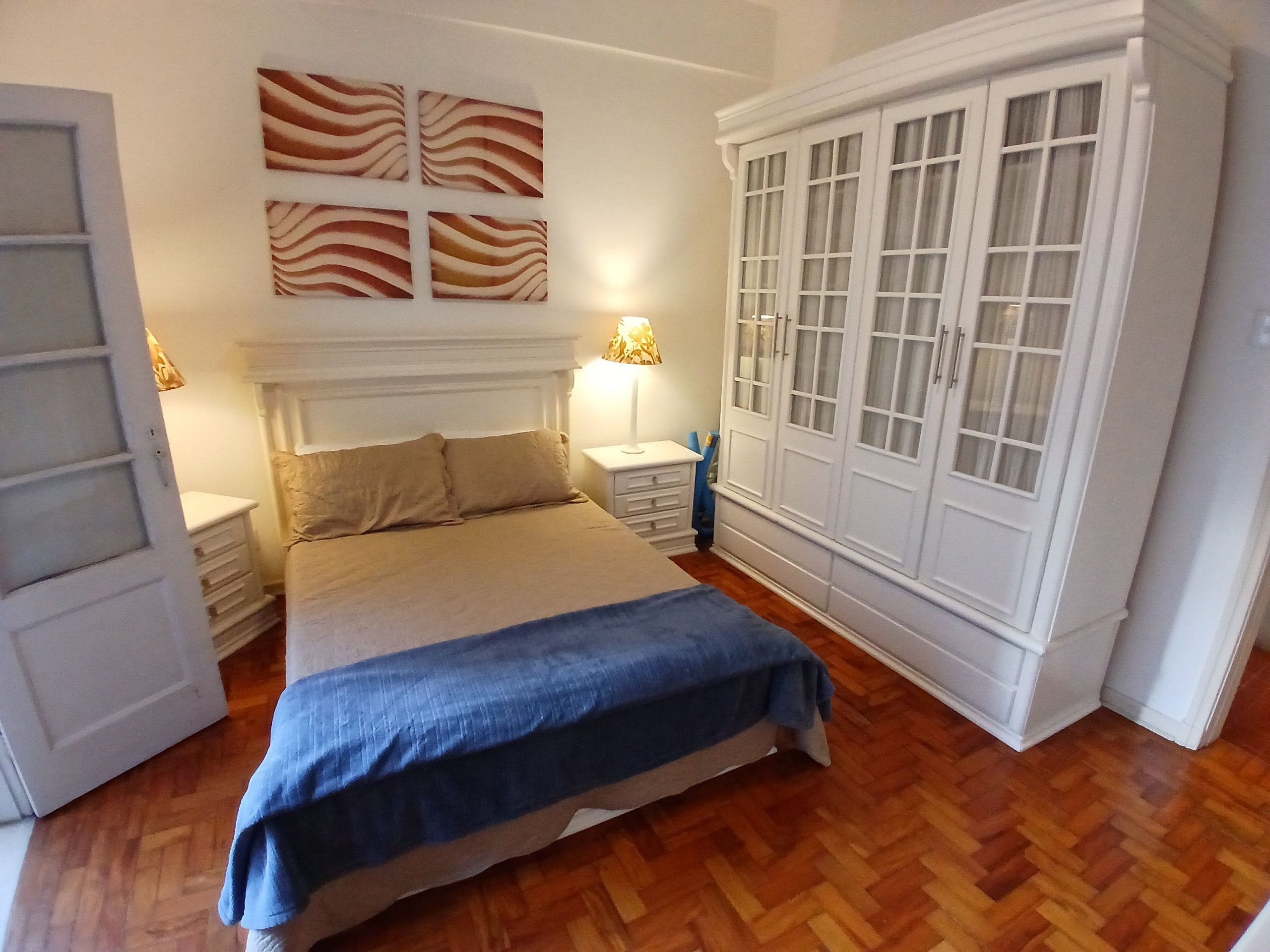A bedroom with a bed, bedside tables, a wardrobe, and wall art.