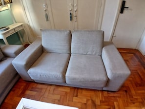 Un sofá gris en una habitación con suelo de madera, un armario blanco y una puerta con picaporte.