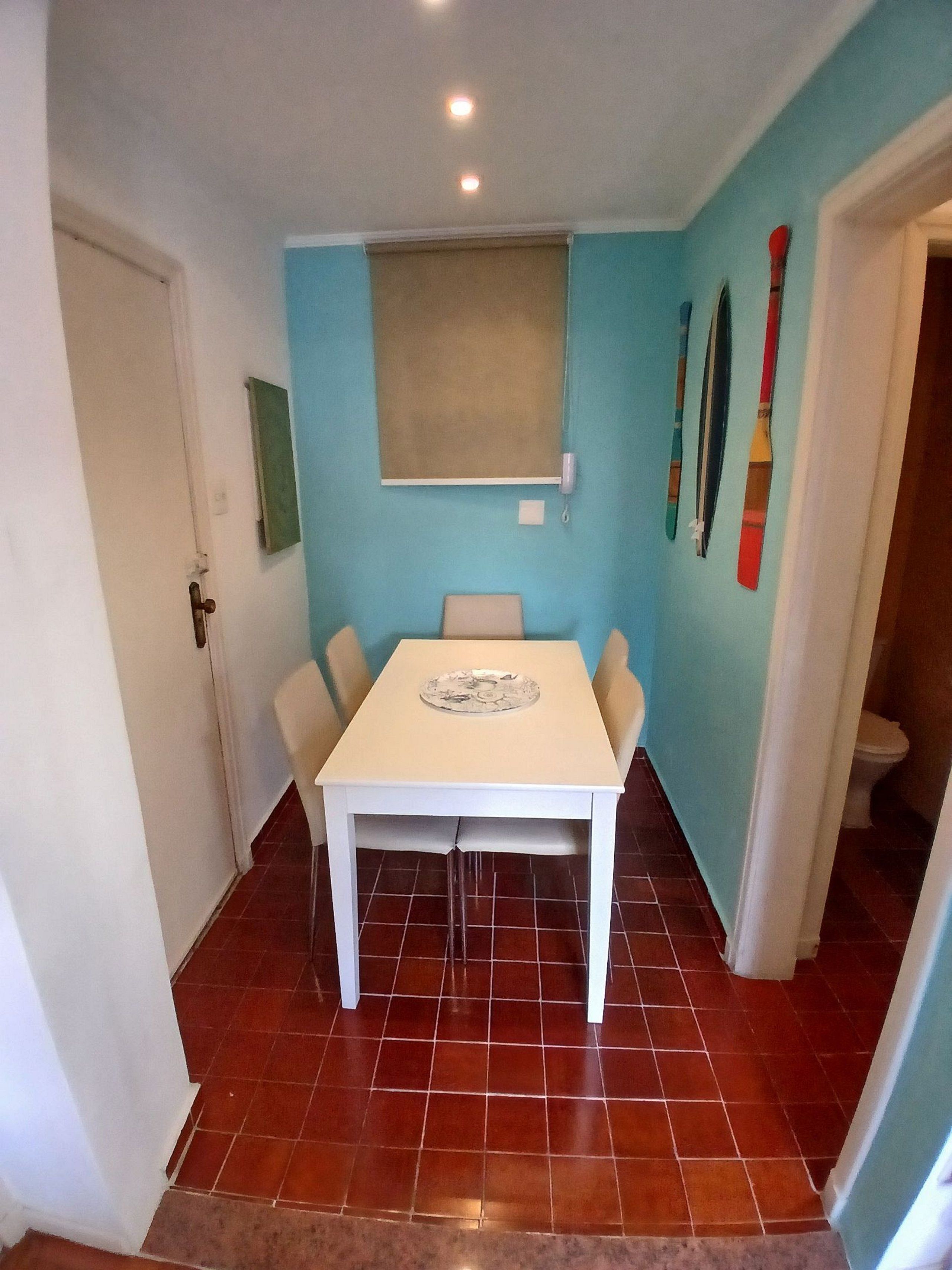 A room with a white table, four chairs, a window with a blind, and a door.