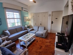 Una sala de estar con sofá, sillón, mesa de centro y mueble para televisión.