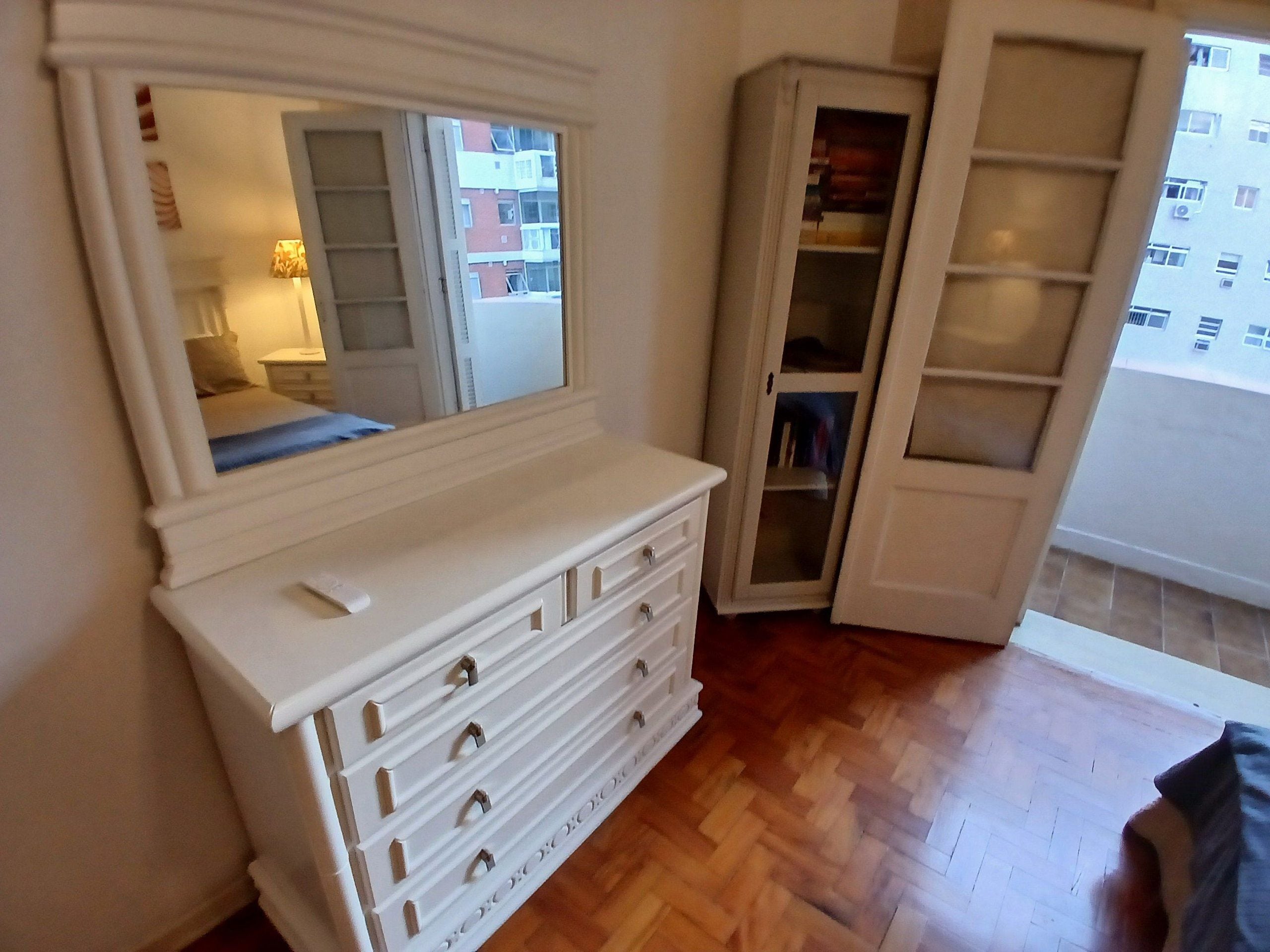 A bedroom with a large mirror, a dresser, a wardrobe, and a wooden floor.