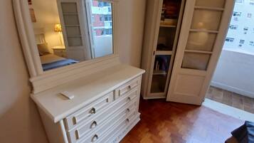 A bedroom with a large mirror, a dresser, a wardrobe, and a wooden floor.