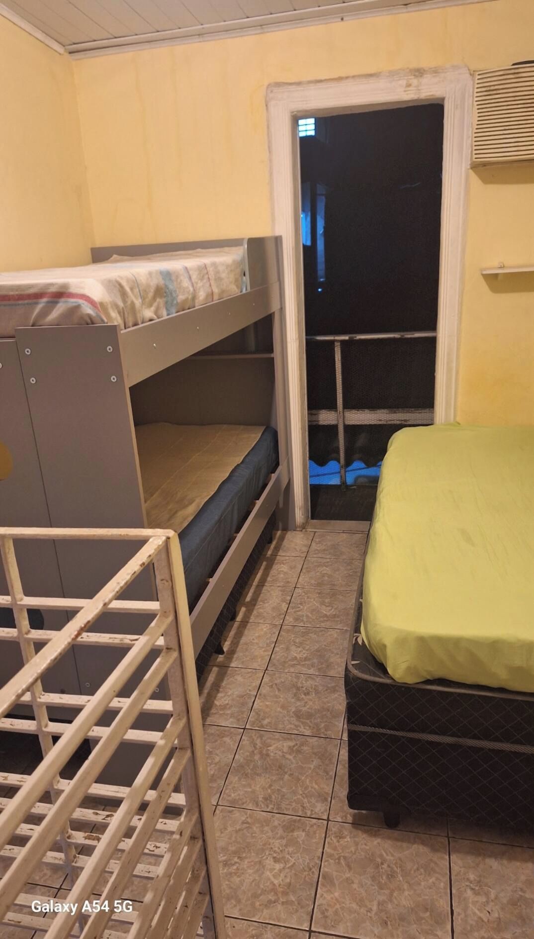Quarto com beliches, uma cama de solteiro, porta para uma varanda e piso em azulejos.
