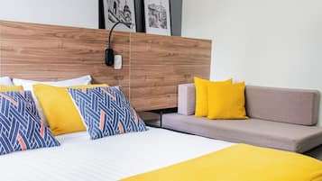 A hotel room with a bed, a sofa, a wall-mounted air conditioner, and two framed pictures.