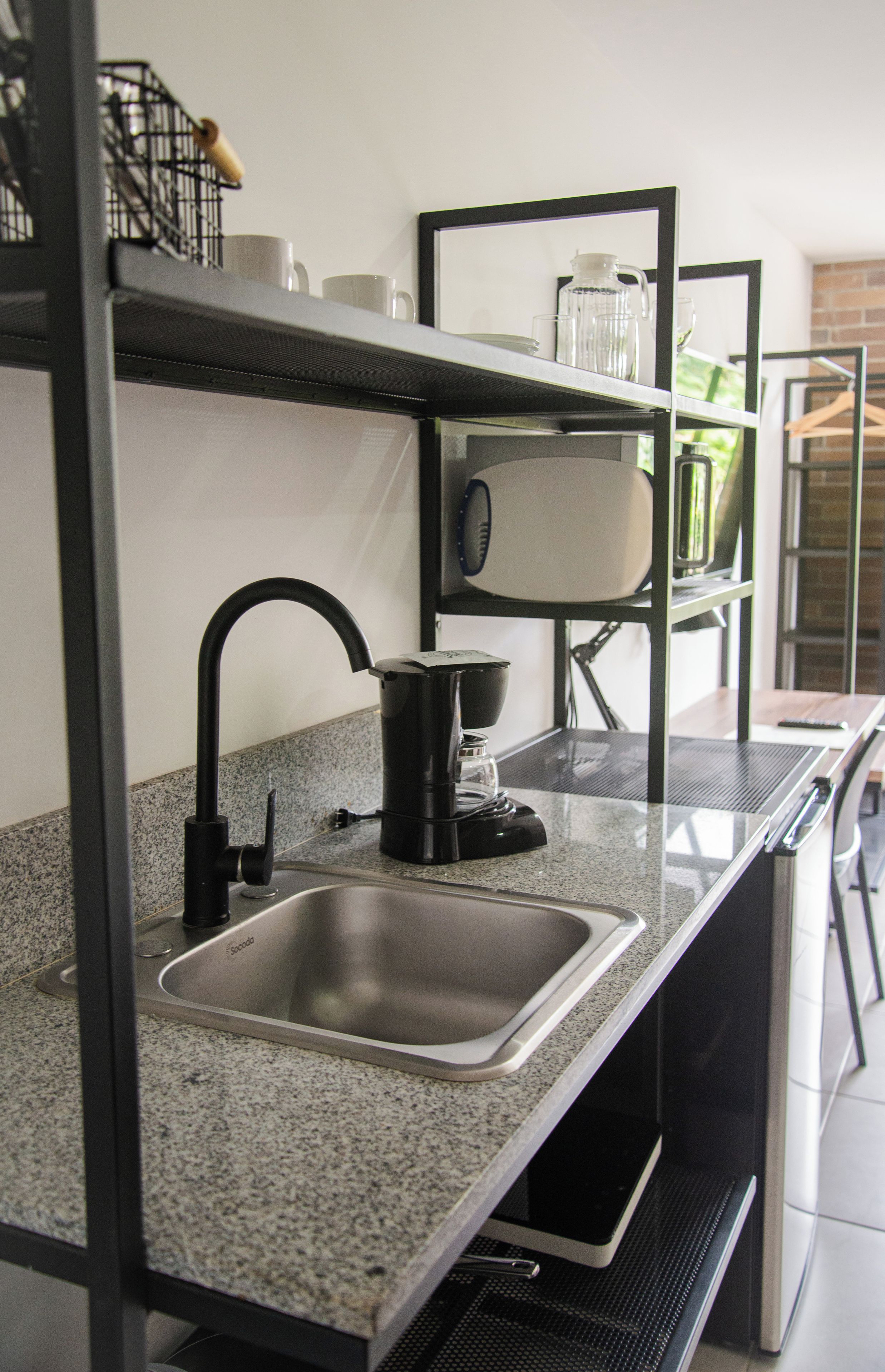 A kitchen with a stainless steel sink, a coffee maker, and a kettle on a granite countertop.