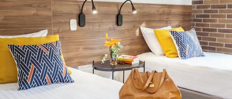 A hotel room with two beds, a small table with a vase of flowers, a book, and a handbag.