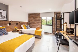 Habitación de hotel con dos camas, un escritorio, una silla, un televisor y una ventana con vista a zonas verdes.