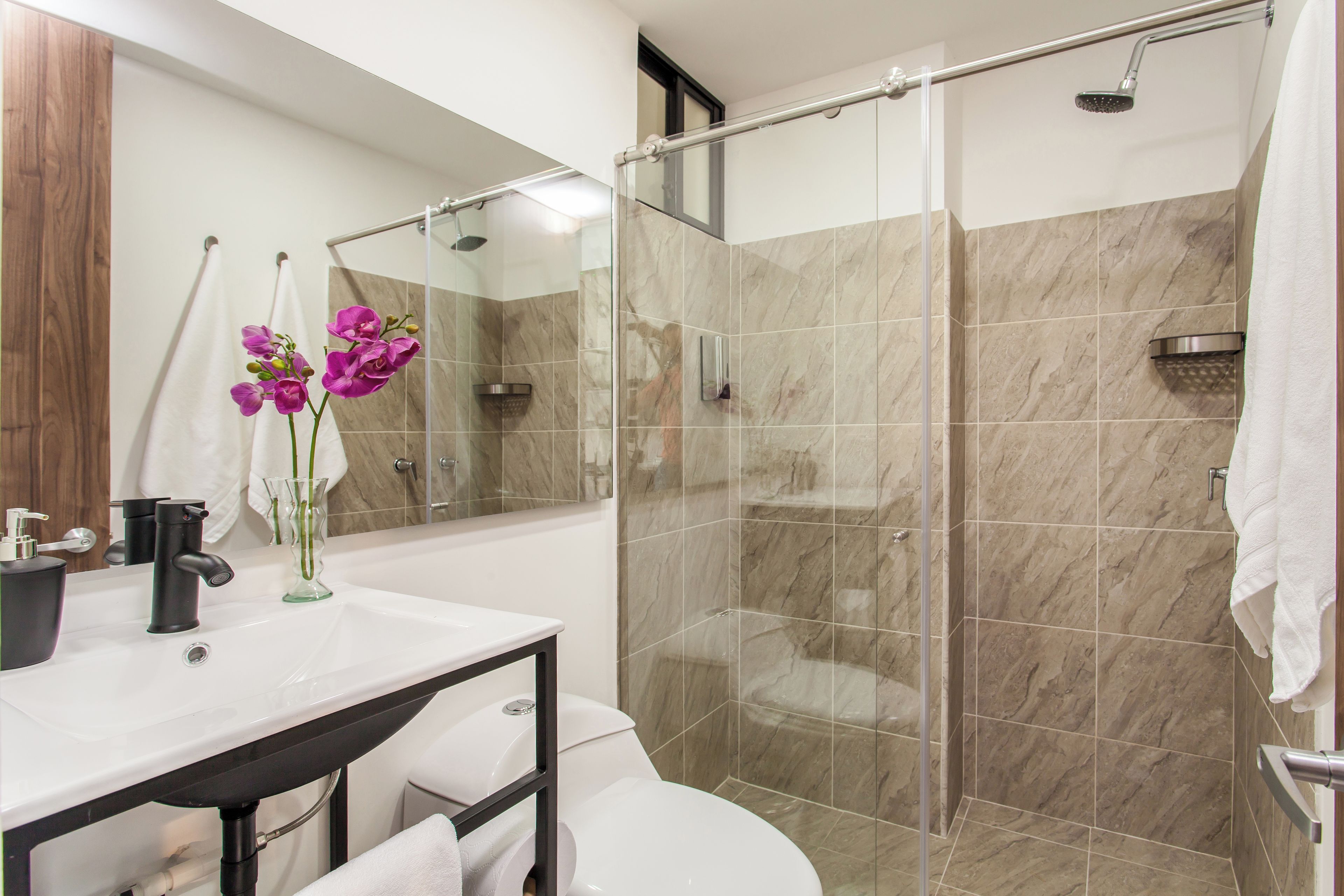 Un baño moderno con cabina de ducha de vidrio, un lavamanos blanco con espejo y un inodoro.