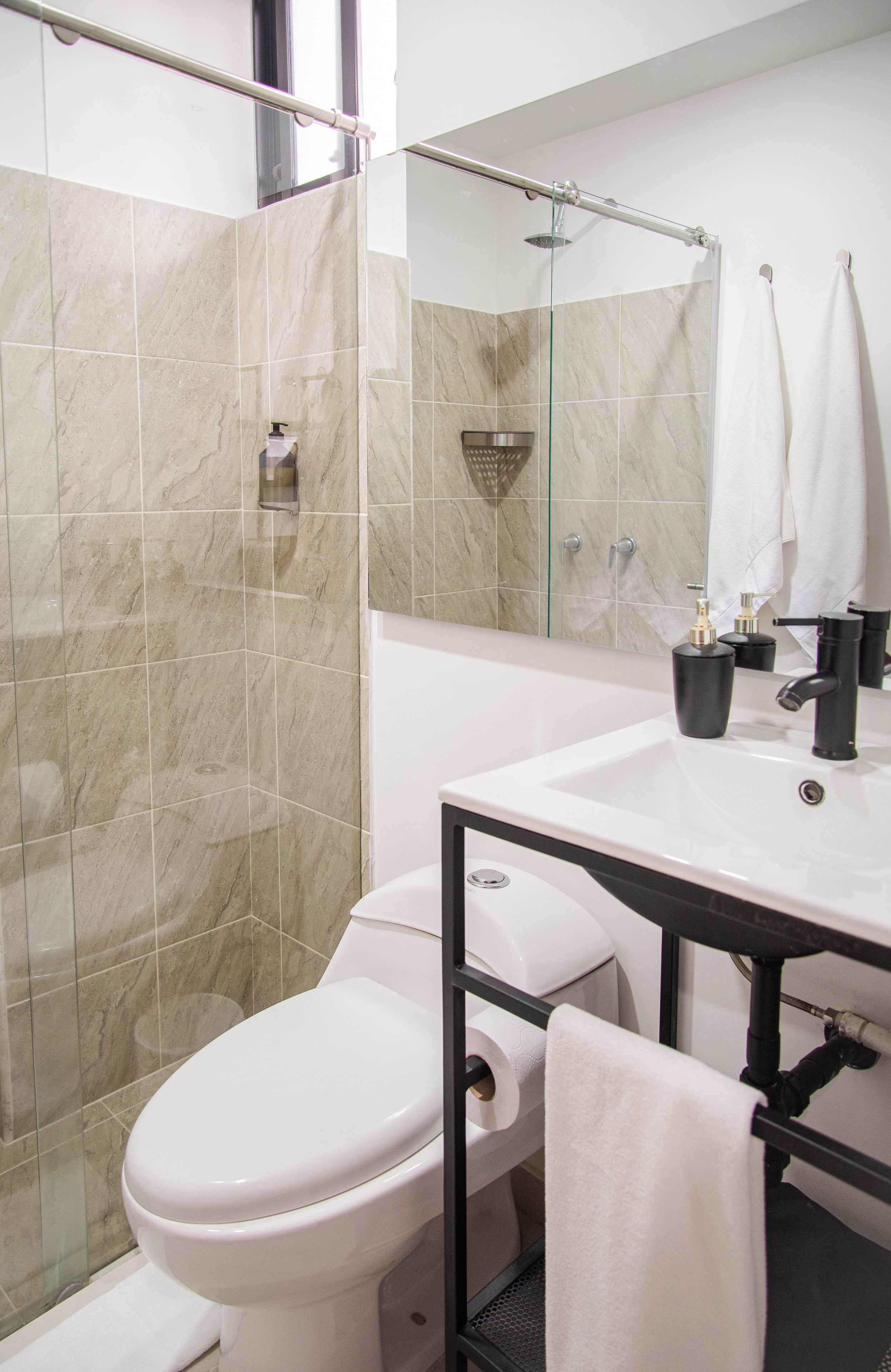 Un baño moderno con inodoro, cabina de ducha de vidrio, lavabo con espejo y perchero para toallas.