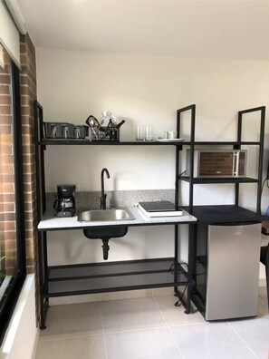 Cocina compacta con lavabo, cafetera, microondas y refrigerador pequeño.