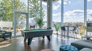 Una mesa de billar en una sala con ventanas amplias, una zona de bar y vista al río.