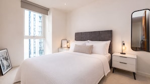 A bedroom with a large bed, bedside tables, a mirror, and a window. - Green Rooms by Veeve (Salford)