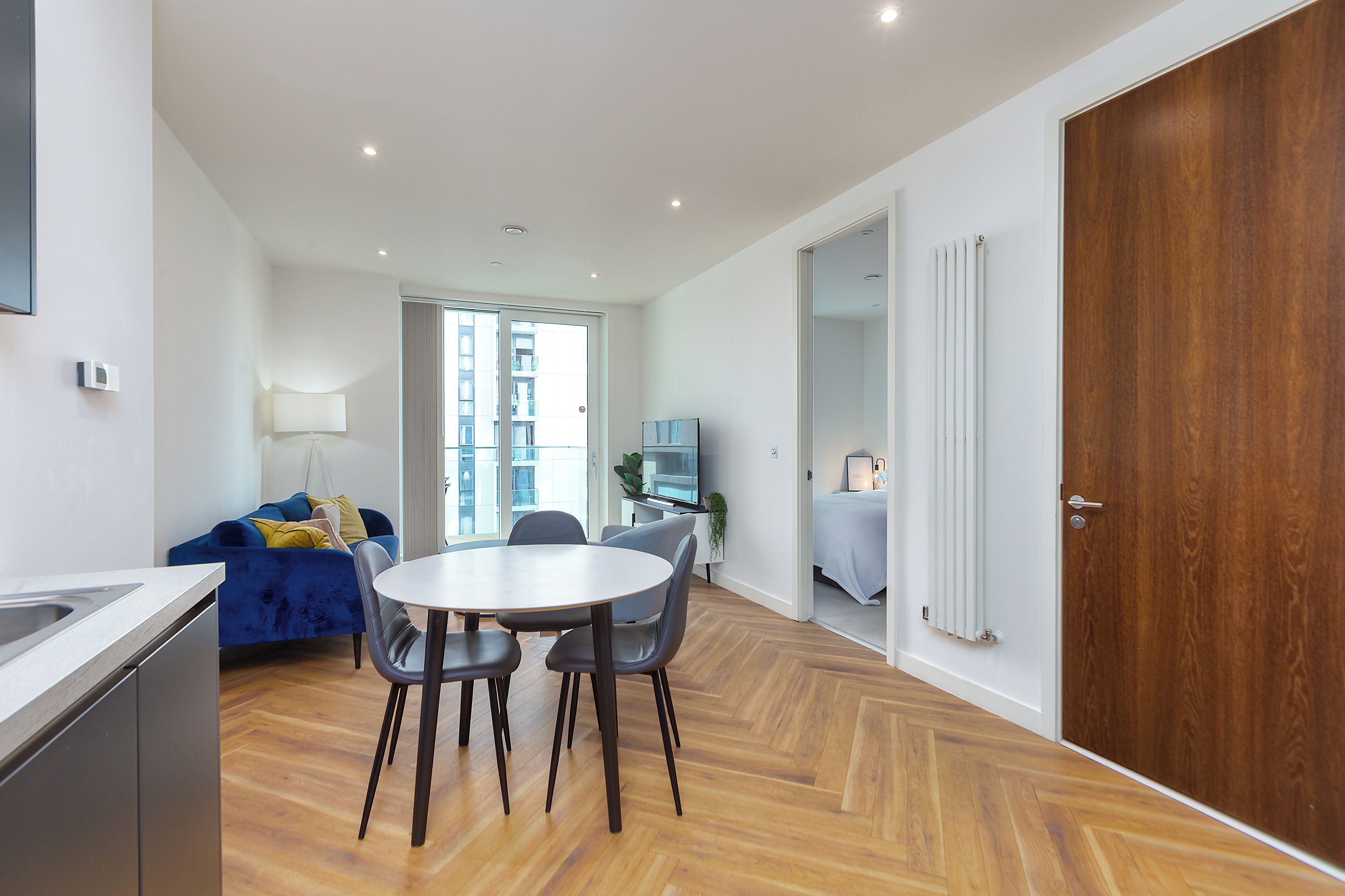 A modern apartment with a dining area, a kitchenette, and a bedroom.