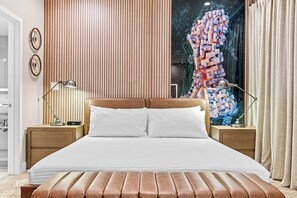 Ein modernes Schlafzimmer mit einem großen Bett, zwei Nachttischen, einem Wandregal, einer an der Wand befestigten Uhr und einem Fenster mit Blick auf eine Stadtlandschaft.
