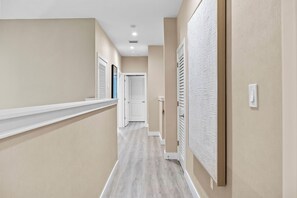 Un couloir avec un plancher en bois, des murs blancs et une porte blanche au fond.