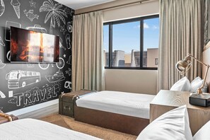 Une chambre d’hôtel avec un lit, un bureau, une fenêtre donnant sur un paysage agréable et un mur décoré sur le thème du voyage.