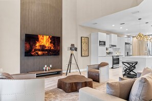 A modern living room with a flat-screen TV, a fireplace, and a kitchen in the background. - 4BR house with hot tub near Disney area (Kissimmee)