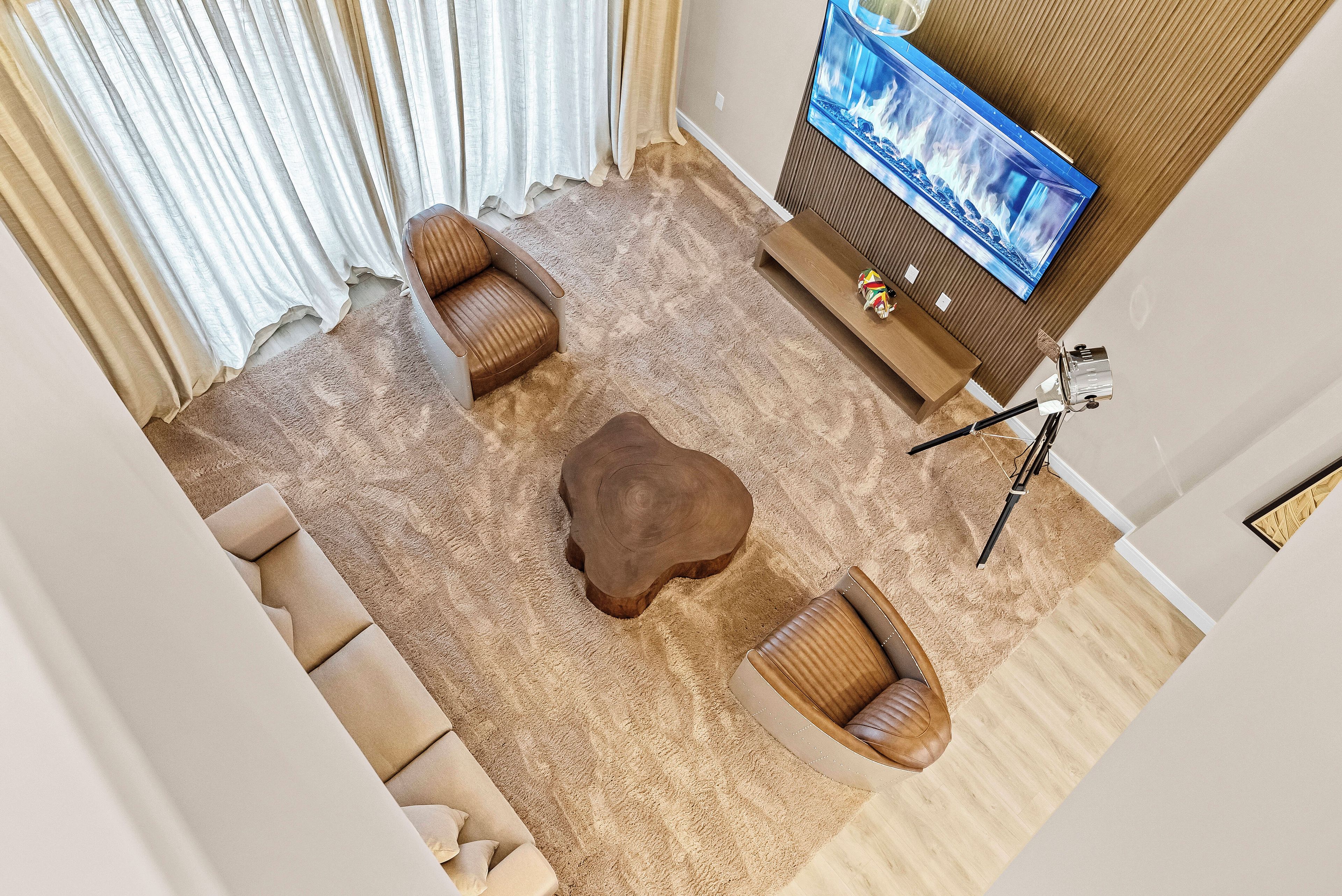 A living room with a flat-screen TV mounted on the wall, a wooden coffee table, two leather sofas, and a tripod with a camera.