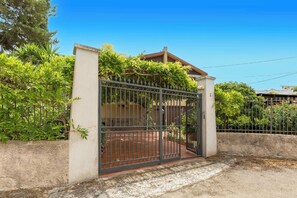 A gated entrance with a metal gate, a concrete wall, and a building with a tiled roof. - Villa Muse by BarbarHouse (Leporano)