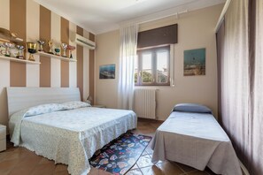 A bedroom with a bed, a smaller bed, a radiator, a window with curtains, and a shelf with trophies. - Villa Muse by BarbarHouse (Leporano)