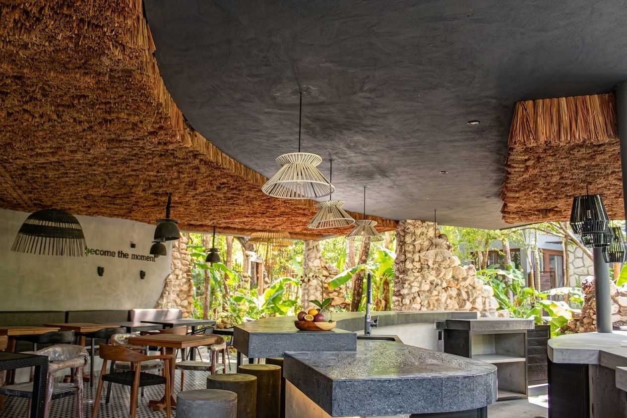 Um espaço de refeições interno com paredes de pedra, móveis de madeira e luminárias pendentes.