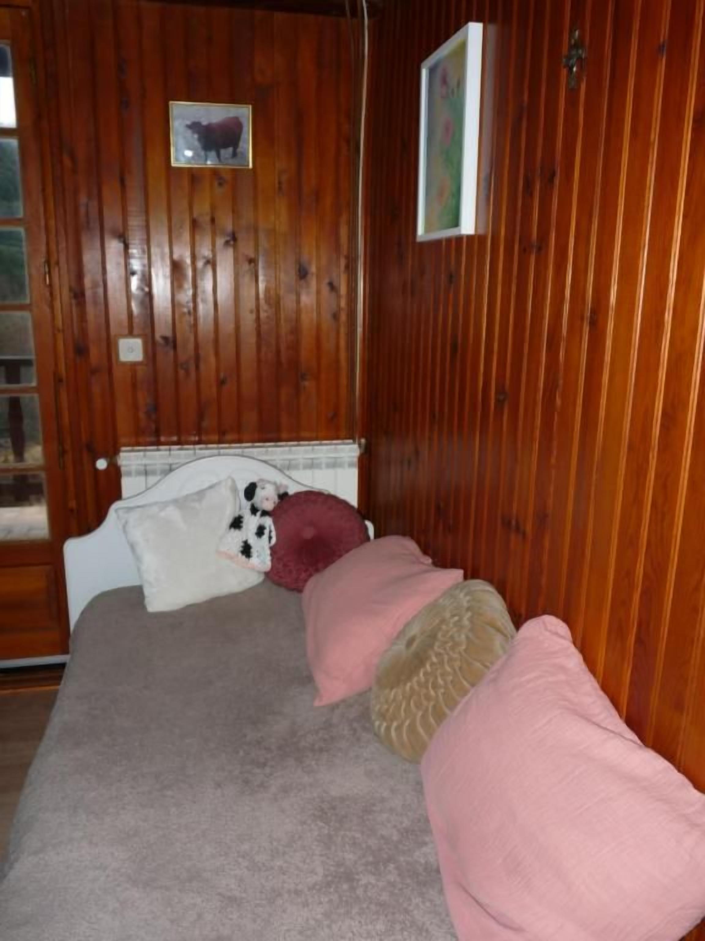 Een kamer met houten lambrisering, een bed, kussens en een lijst met een afbeelding erop.