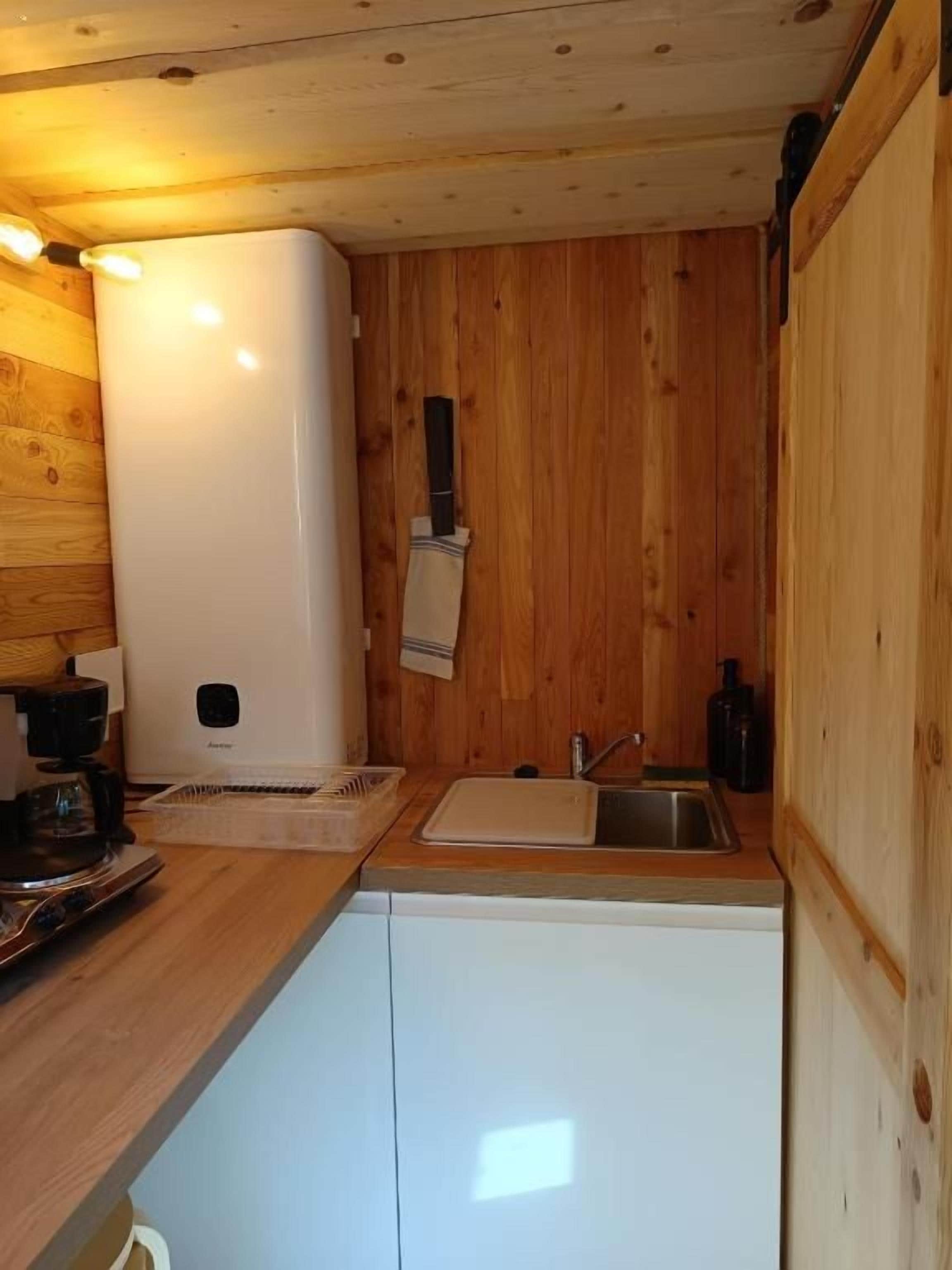 Une cuisine compacte aux murs en bois, avec un réfrigérateur blanc, un évier et une machine à café.