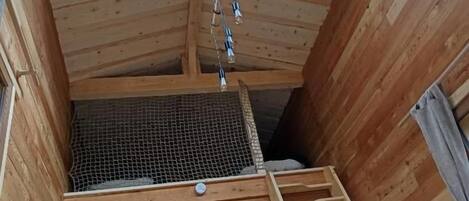 Interior de madera con tragaluz, escalera y una zona pequeña cerrada con techo de malla.