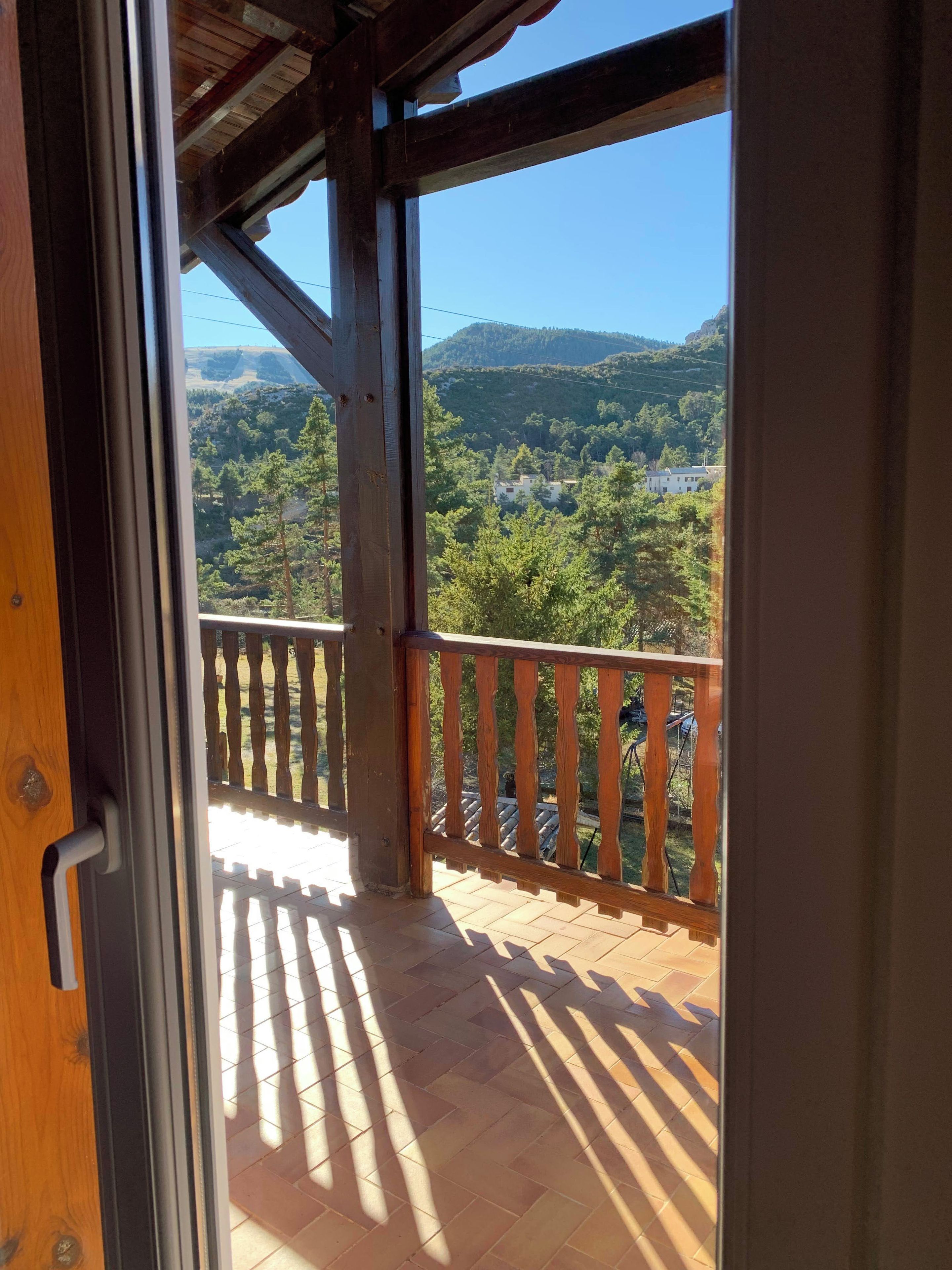 Un balcón de madera con vistas a un paisaje montañoso y una zona residencial.