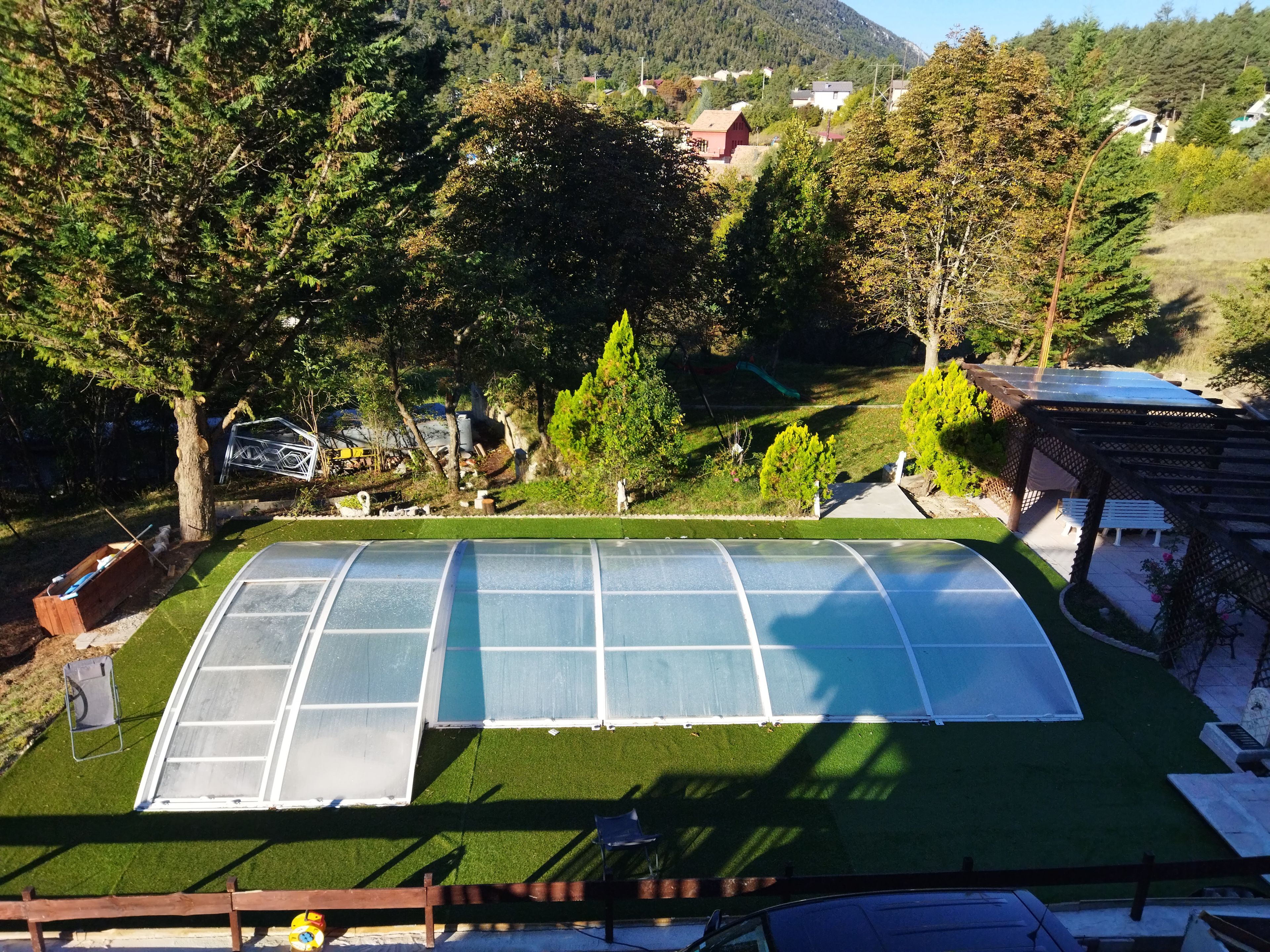 Une serre dotée d’une toiture transparente, entourée d’une pelouse bien entretenue et d’arbres.