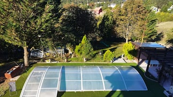 Une serre dotée d’une toiture transparente, entourée d’une pelouse bien entretenue et d’arbres.