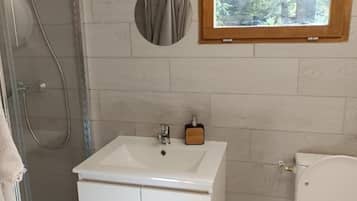 Un baño con ducha, lavamanos, inodoro y ventana con vistas a árboles.