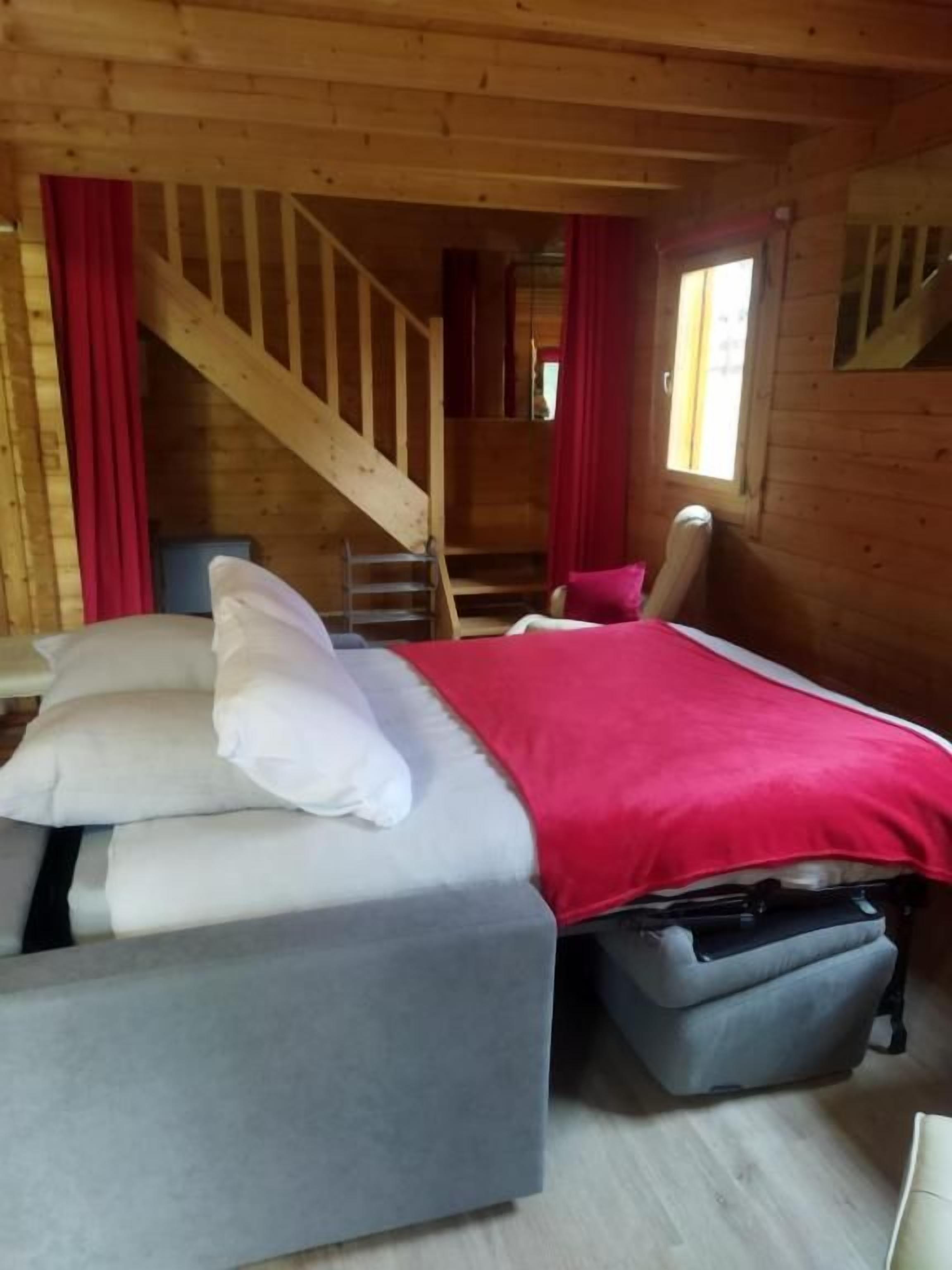 Een houten cabinneerinrichting met een bed, een stoel, een trap en een raam.