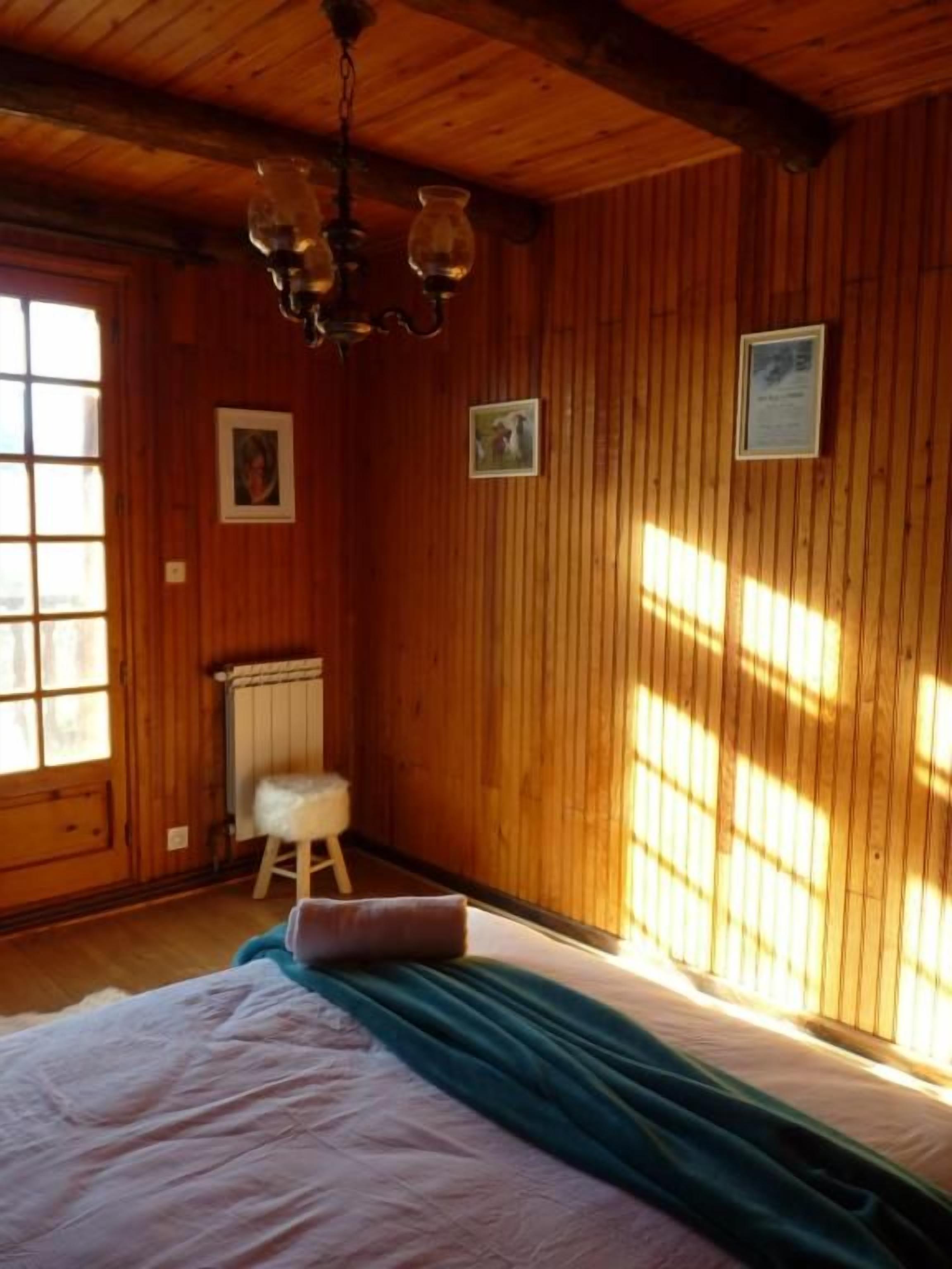 A room with wooden walls, a bed with a green blanket, a white radiator, and a small stool.