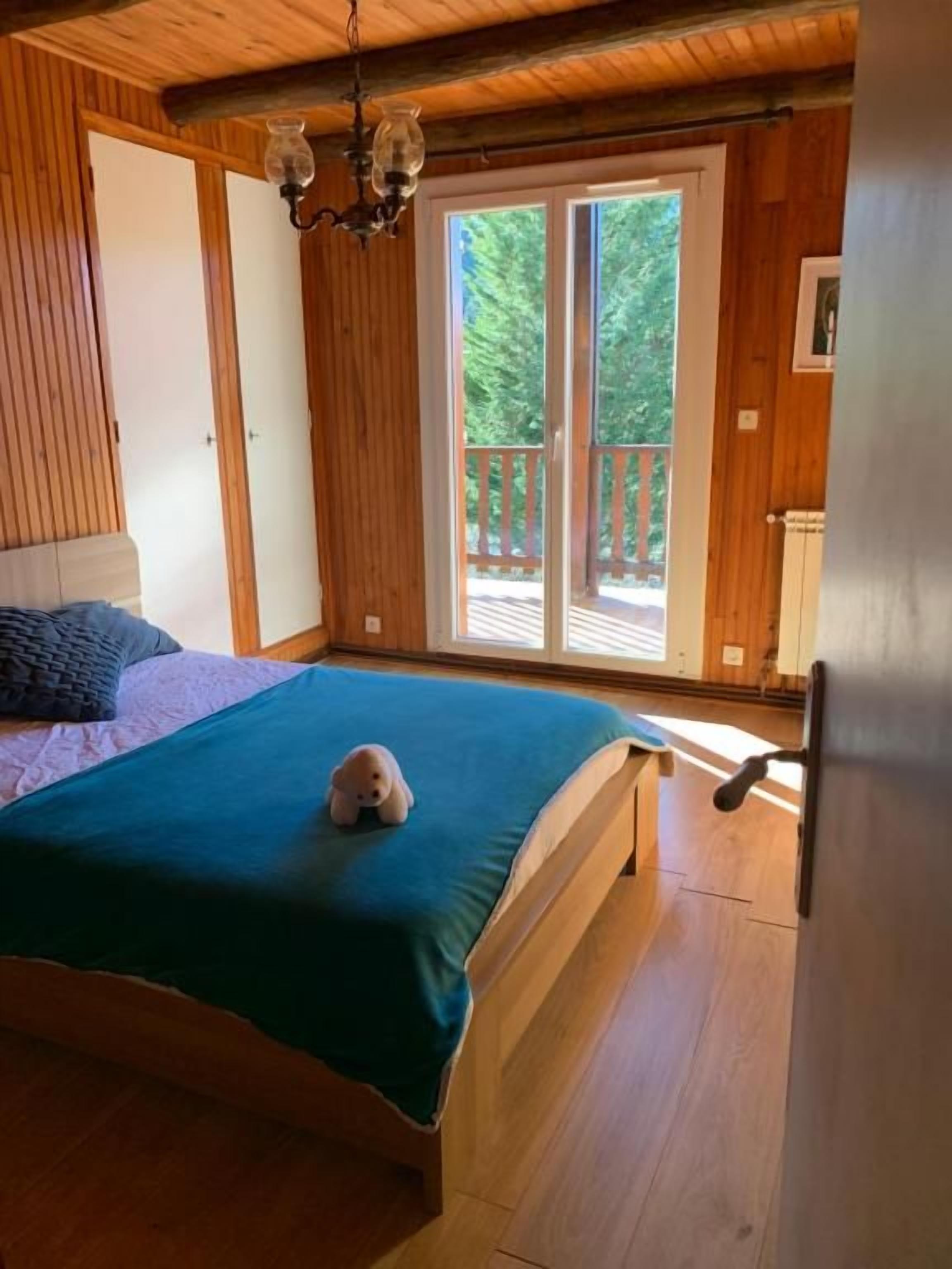 Ein Schlafzimmer einer Holzhütte mit einem Bett, einer kleinen Bär-Dekoration und einer Schiebetür zum Balkon.