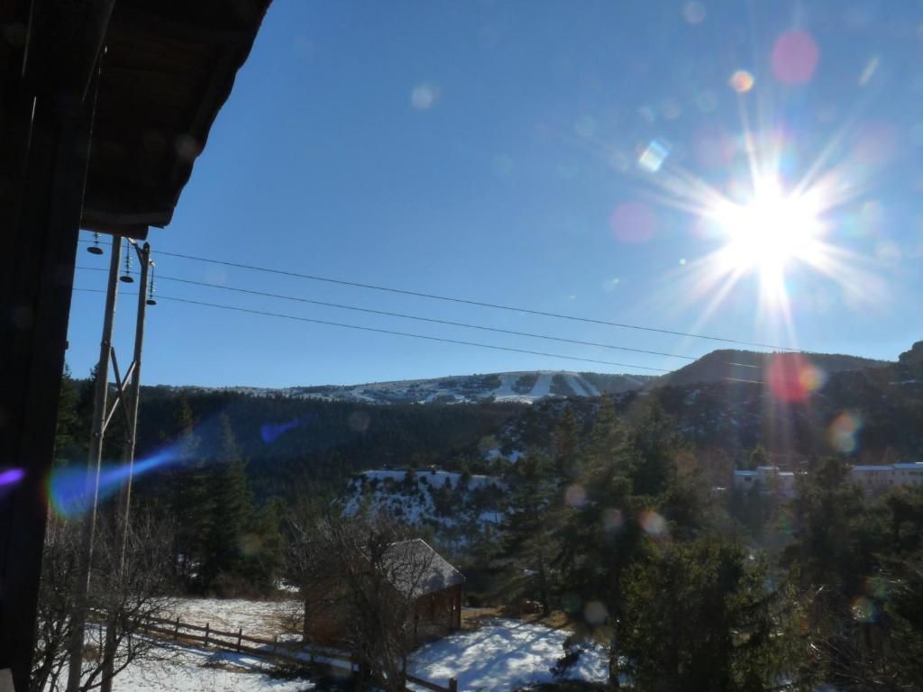 A clear sky with a bright sun, a snow-covered landscape, and a wooden cabin.