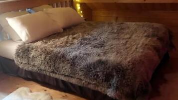 A wooden cabin interior with a bed, pillows, and a fur rug on the floor.