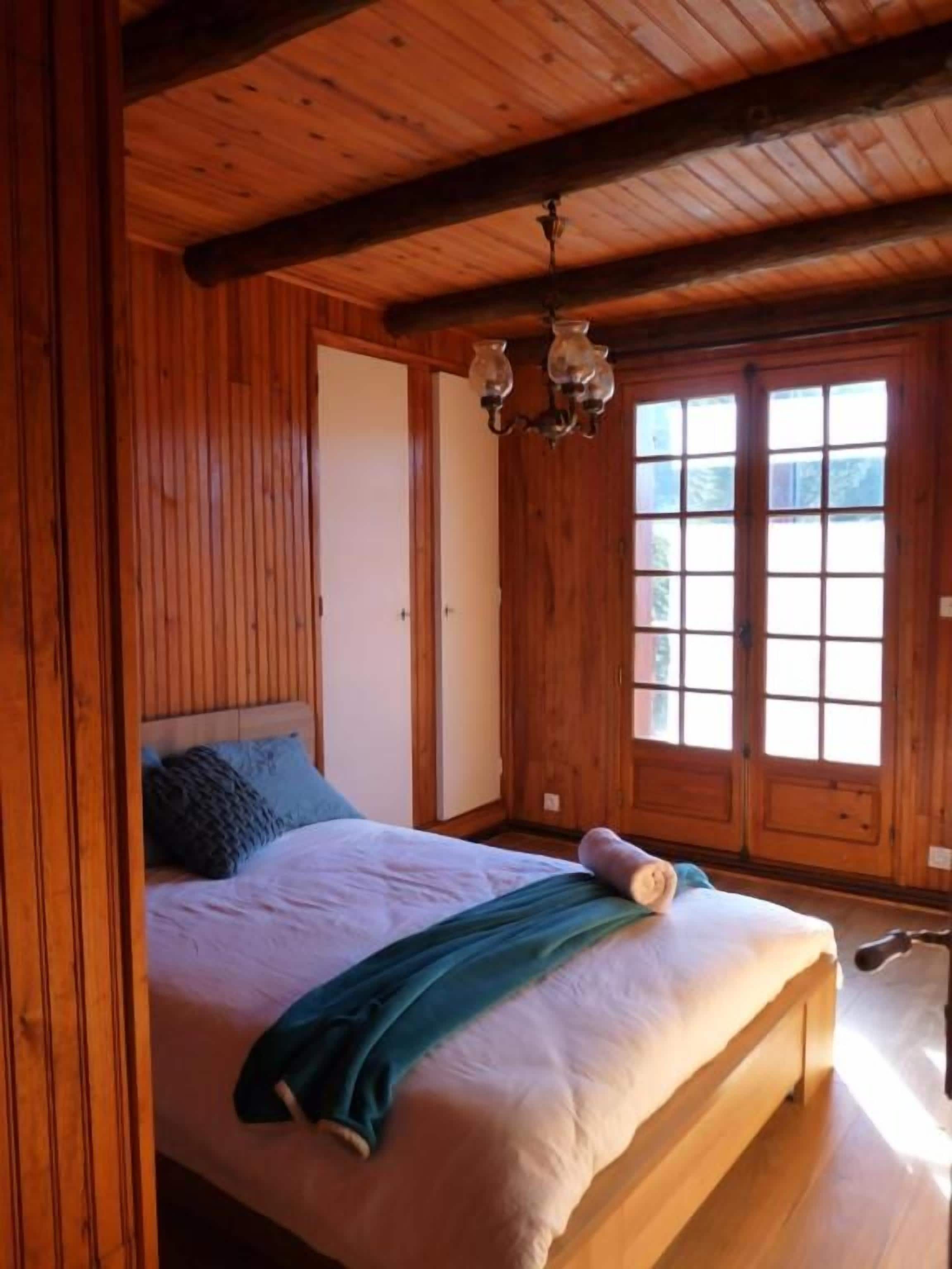 A wooden-paneled bedroom with a bed, a chandelier, and a large window.
