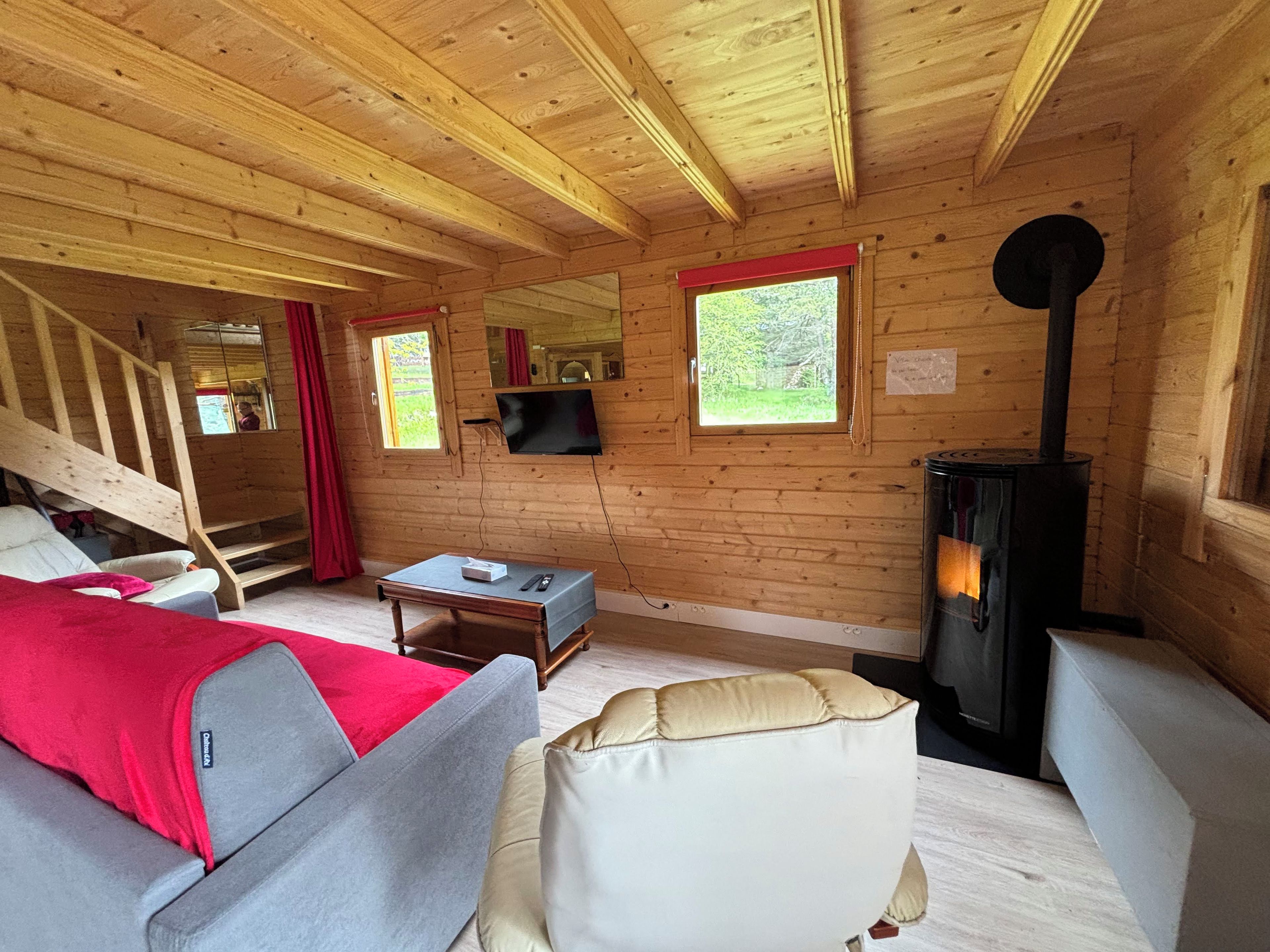 L’intérieur d’un chalet en bois, avec un canapé, une table, un téléviseur, une cheminée et un escalier.