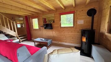 L’intérieur d’un chalet en bois, avec un canapé, une table, un téléviseur, une cheminée et un escalier.