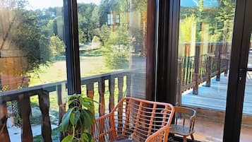 Ein Balkon mit einem Korbstuhl, einem Blumentopf und Blick auf einen Garten und Bäume.