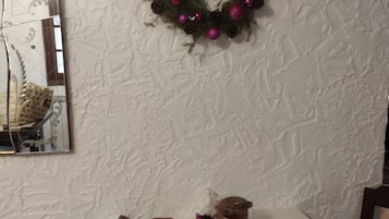 Ein Esstisch mit einer Speiseplatte, einer Tasse und einem Glas dunkler Flüssigkeit, möglicherweise Kaffee, an einer strukturierten weißen Wand mit einem dekorativen Kranz darüber.