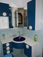 Un baño con un lavamanos azul, armarios blancos y un espejo.