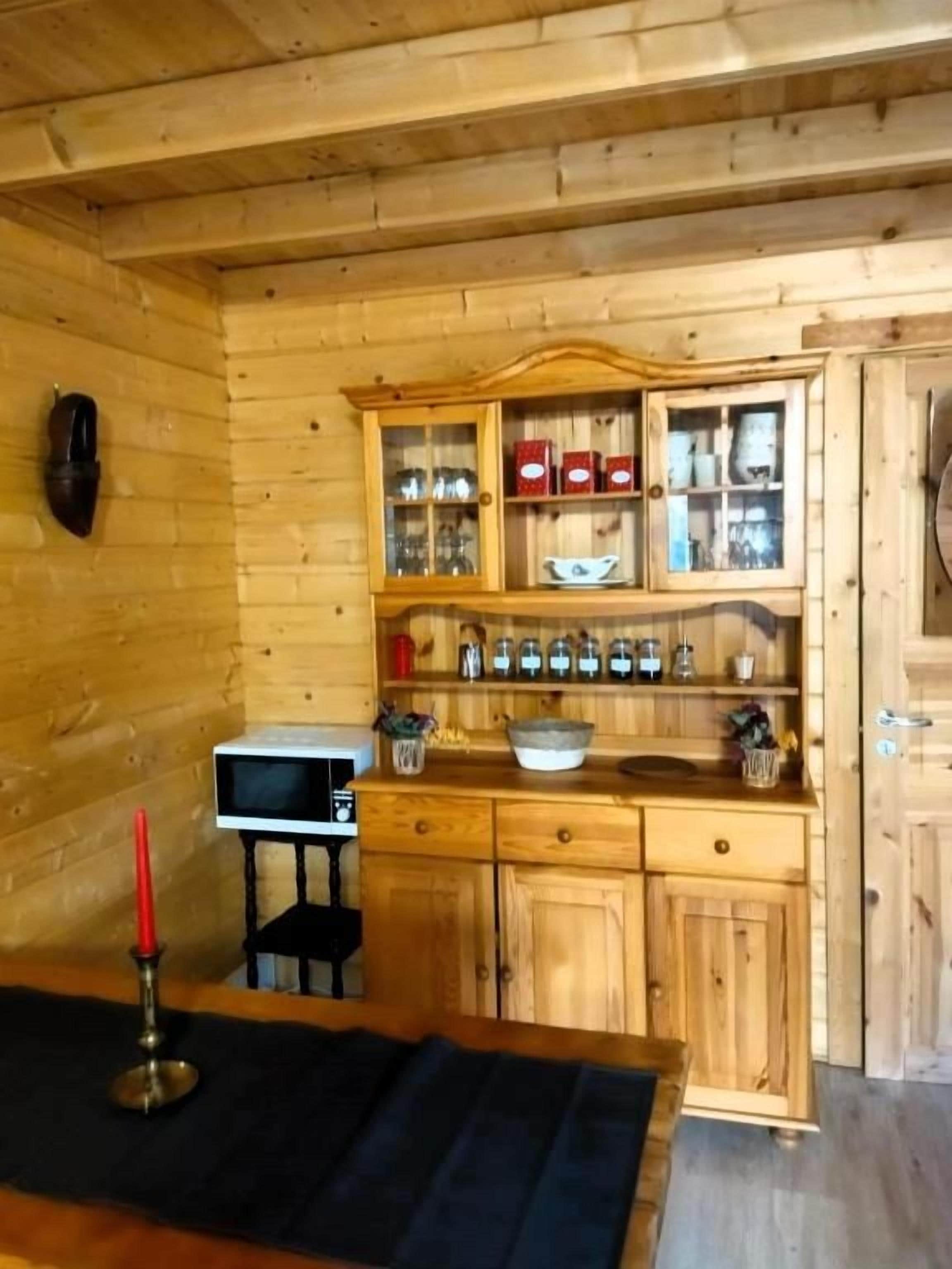 Un intérieur en bois comprenant un coin cuisine, avec des placards, un four à micro-ondes et une table à manger agrémentée d’un chandelier.