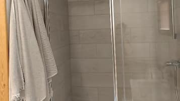 Un espace douche doté d’une porte en verre, d’un mur recouvert de carreaux blancs et d’un porte-serviettes avec des serviettes.